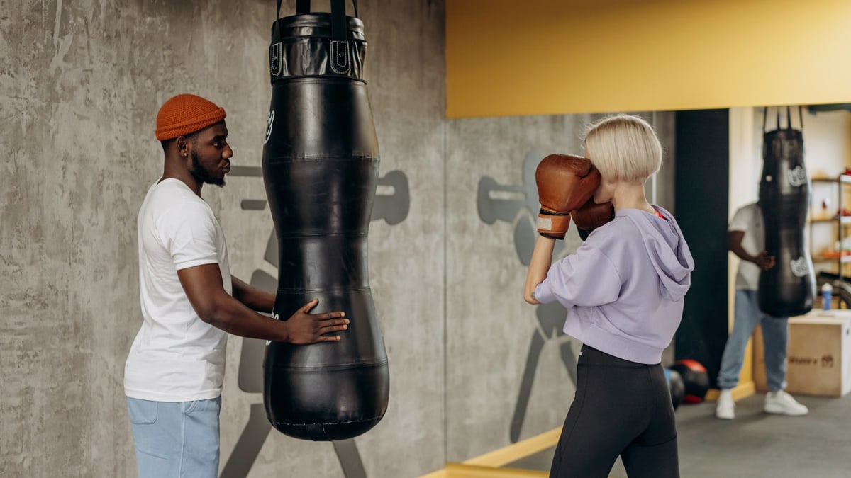A woman practicing boxing with a coach in an indoor gym setting, focused on a training session.